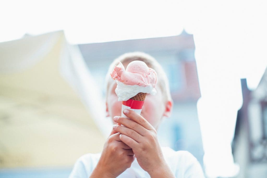A young boy puts an ice cream cone in front of his face.