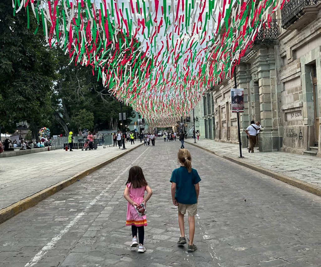 Two kids walking under street decorations of the Mexican flag in Oaxaca, Mexico