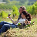A couple lounging in a field in Napa Valley sipping on a glass of wine.