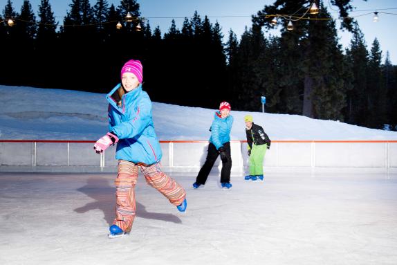 Three kids ice skating at Tahoe City Winter Sports Park.