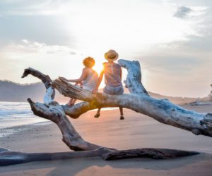 Two kids sitting on a tree branch on a beach in Costa Rica.