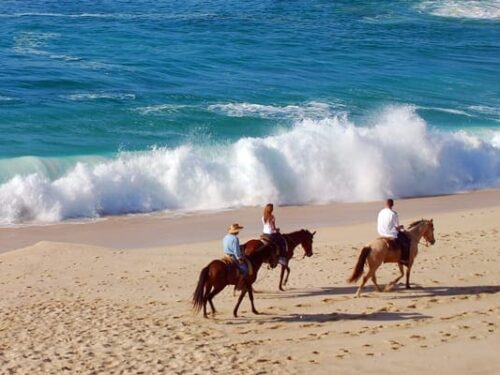 Family of three riding horses on a beach with crashing waves in Los Cabos Mexico