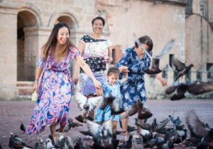A multigenerational group of women dances in a courtyard with pigeons in Santo Domingo.