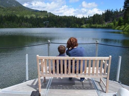 Whistler With Kids. Mom and son sit on bench overlooking a lake in Whistler Vacation Families